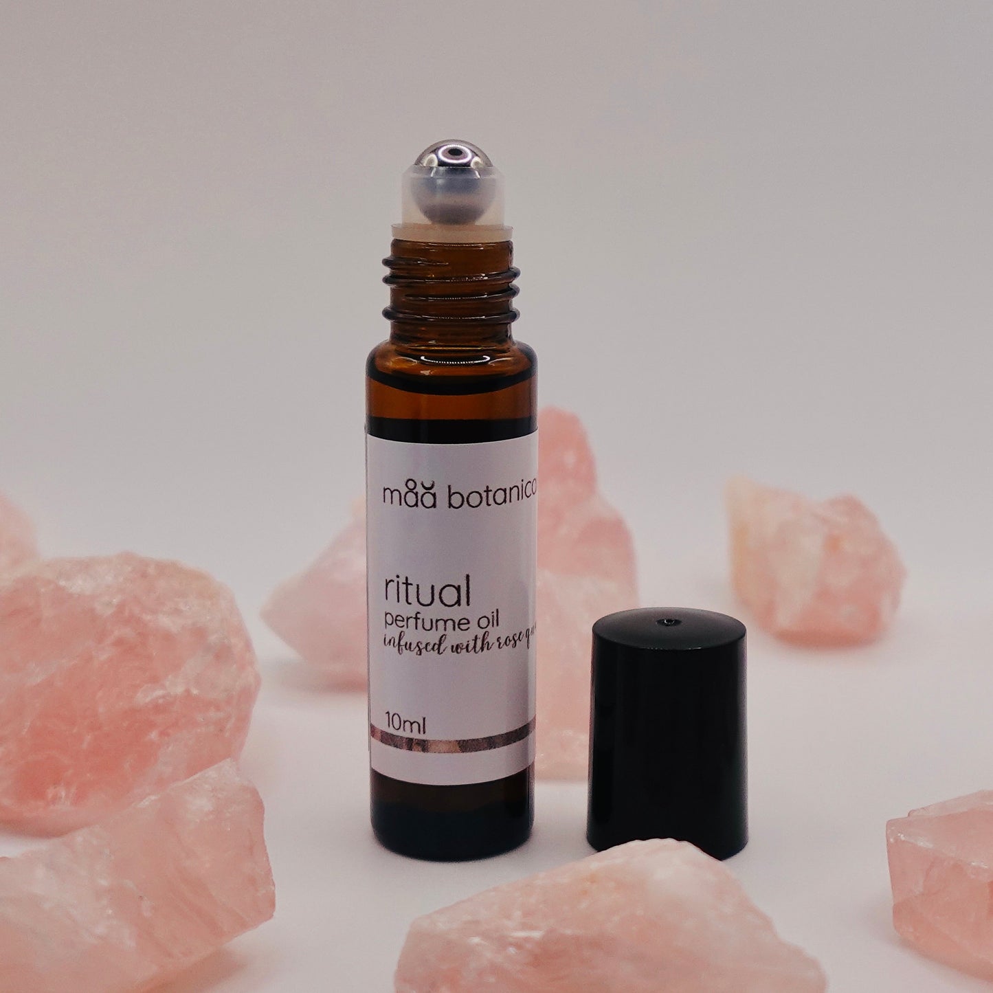 Amber roll-on bottle of maa botanicals ritual perfume oil surrounded by rose quartz crystals