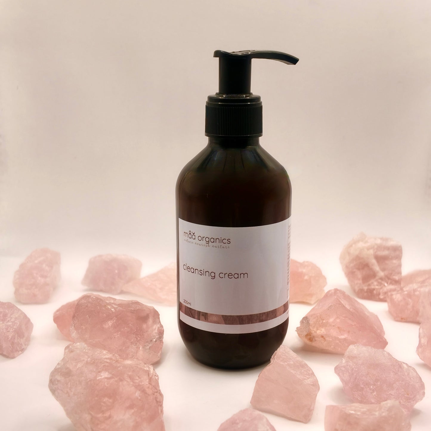 maa botanicals cleansing cream in a 200ml amber bottle with black pump surrounded by rose quartz crystal