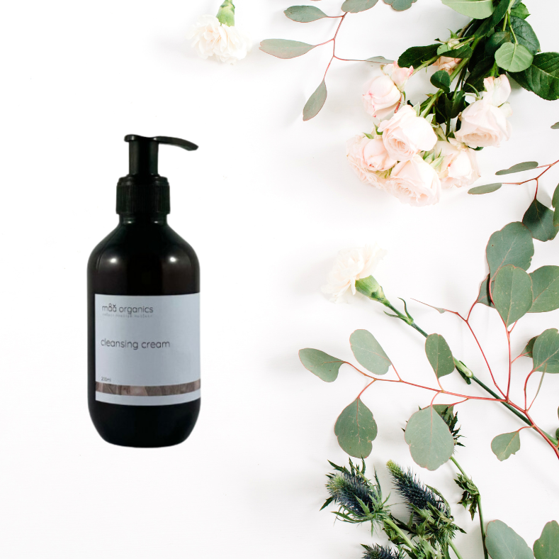 Amber bottle of cleansing cream with a label on a white background with greenery.