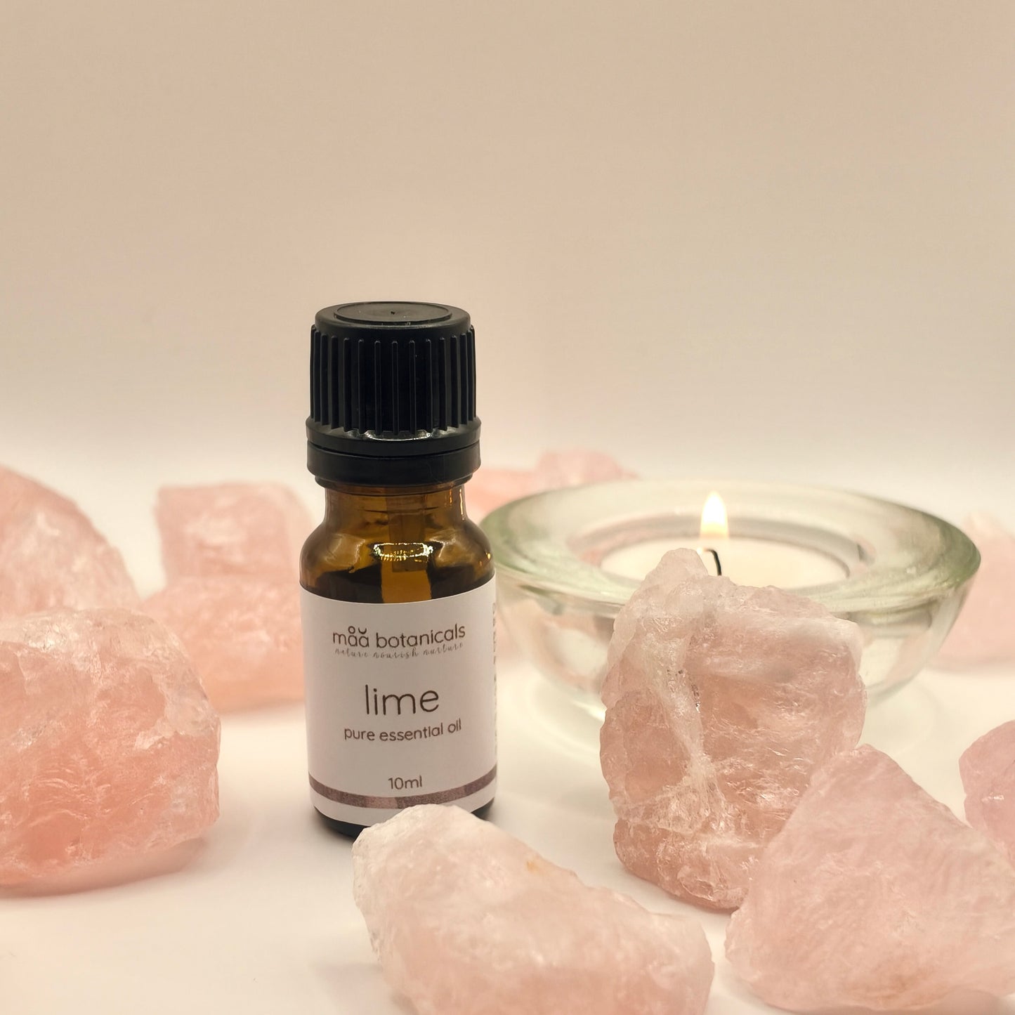 lime essential oil in a 10ml amber bottle surrounded by rose quartz crystal and a tealigt candle