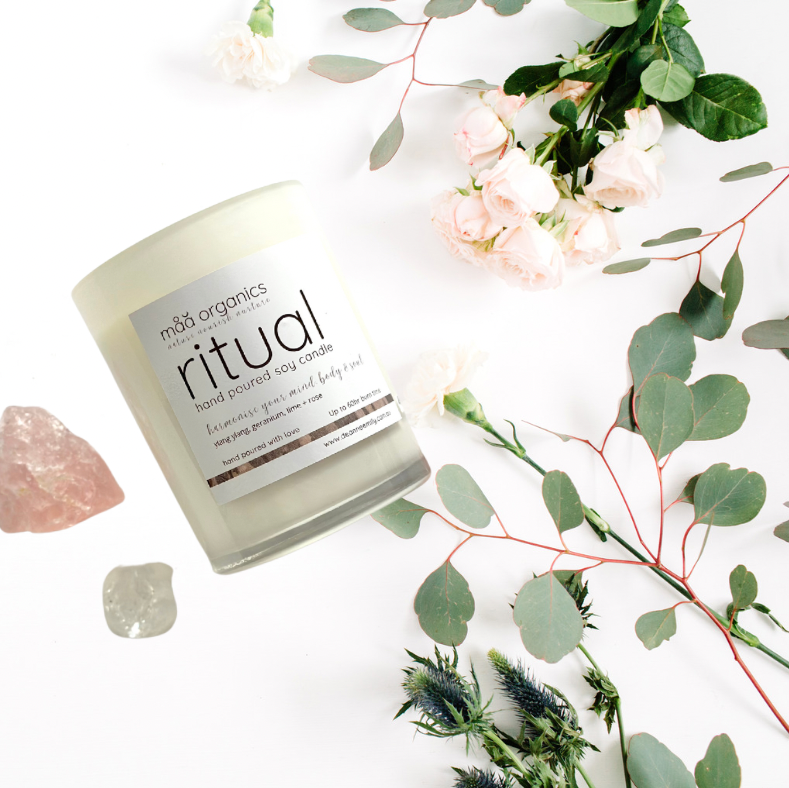 Candle labeled 'ritual' with flowers and crystals on a white background