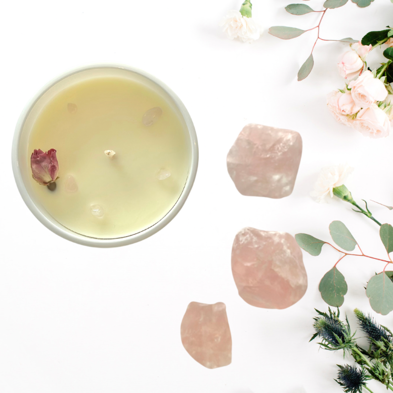 Candle in a white container with pink stones and flowers on a light background