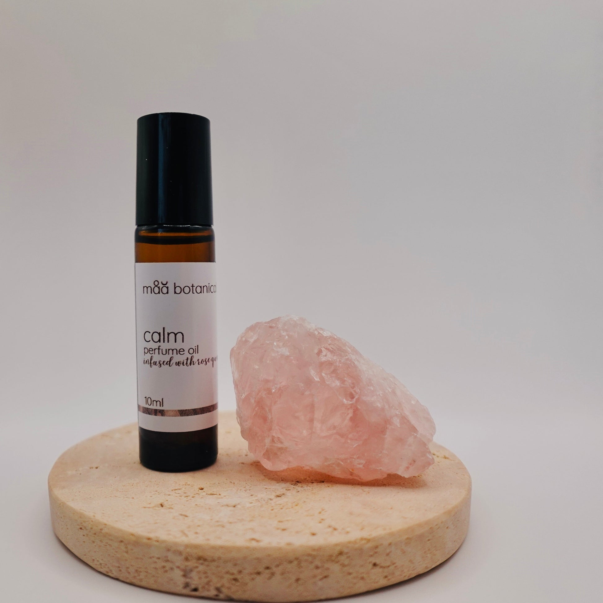maa botanicals calm perfume oil on a stone stand with a rose quartz crystal.