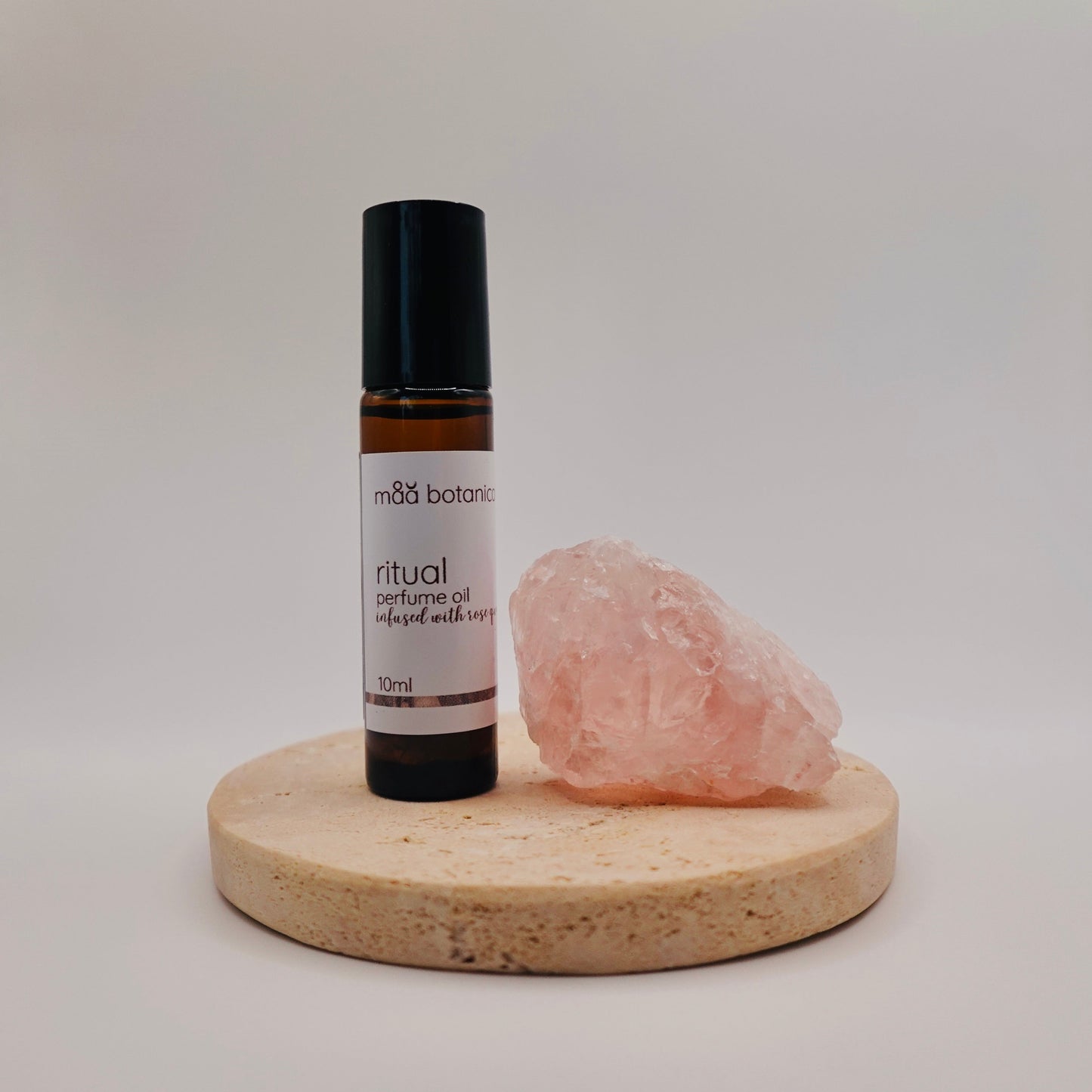 Roll-on perfume bottle labeled 'ritual' with a rose quartz crystal on a stone stand against a white background