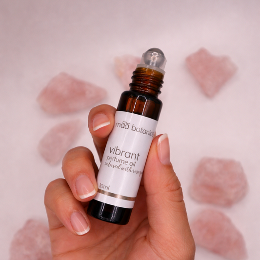 Hand holding a bottle of vibrant perfume oil with rose quartz crystals