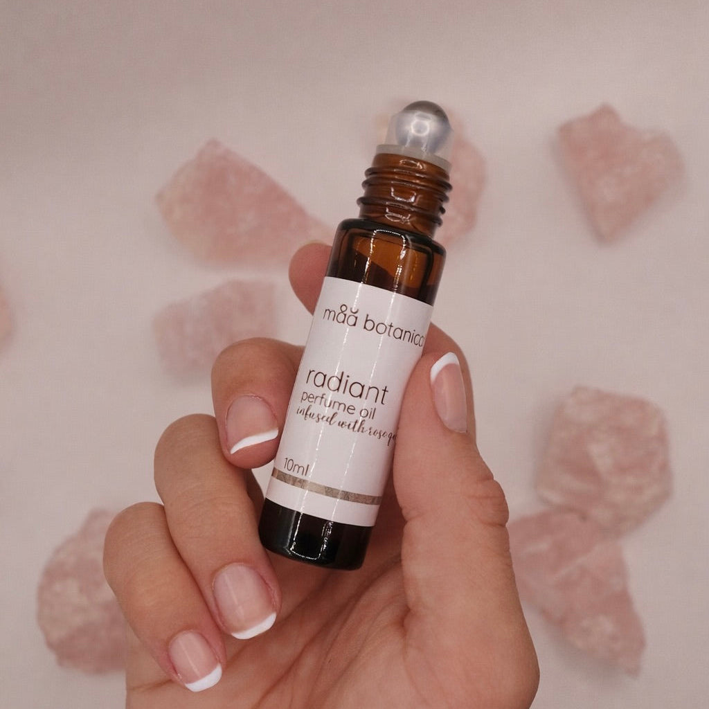 Hand holding anmaa botanicals radiant perfume oil bottle against a soft pink background