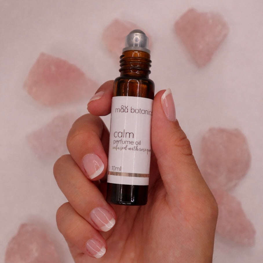 Hand holding maa botanicals calm perfume oil with rose quartz crystals in the background