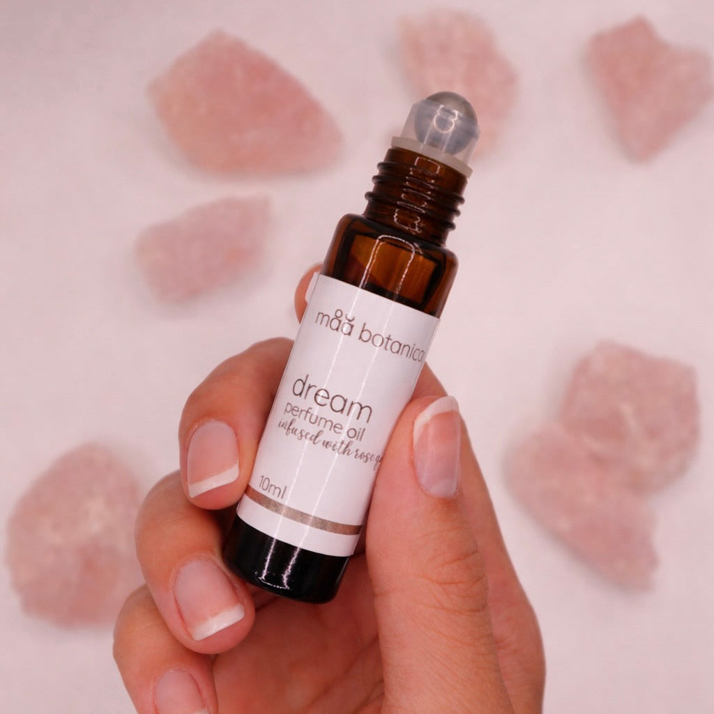 Hand holding a bottle of maa botanicals dream perfume oil with rose quartz crystals in the background