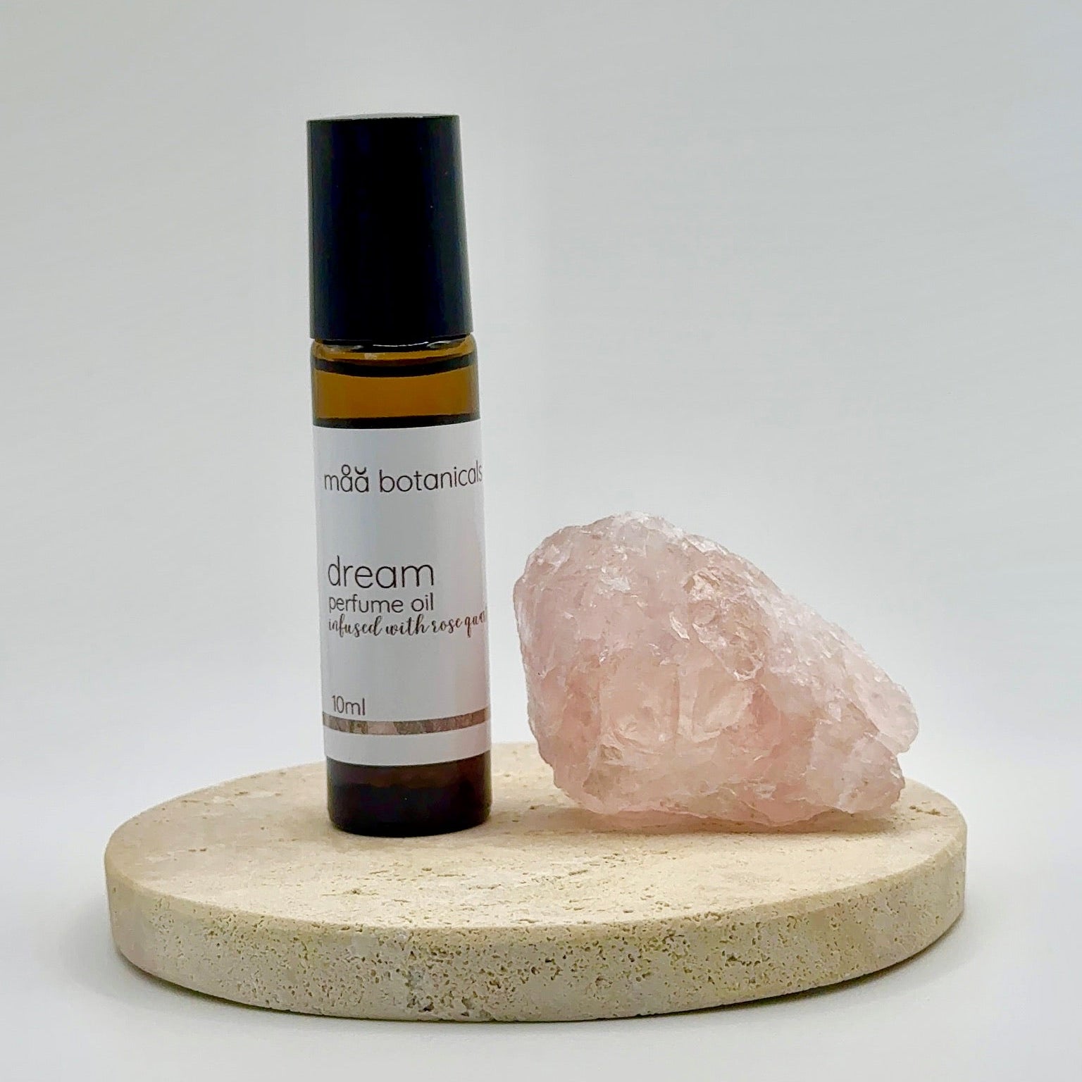 maa botanicals dream roll-on perfume oil om a stone stand with a rose quartz  crystal 