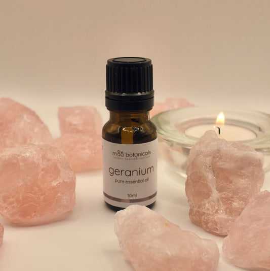geranium essential oil in a 10ml amber bottle surrounded by rose quartz crystal and a tealigt candle