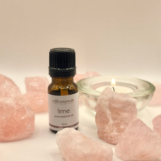 lime essential oil in a 10ml amber bottle surrounded by rose quartz crystal and a tealigt candle