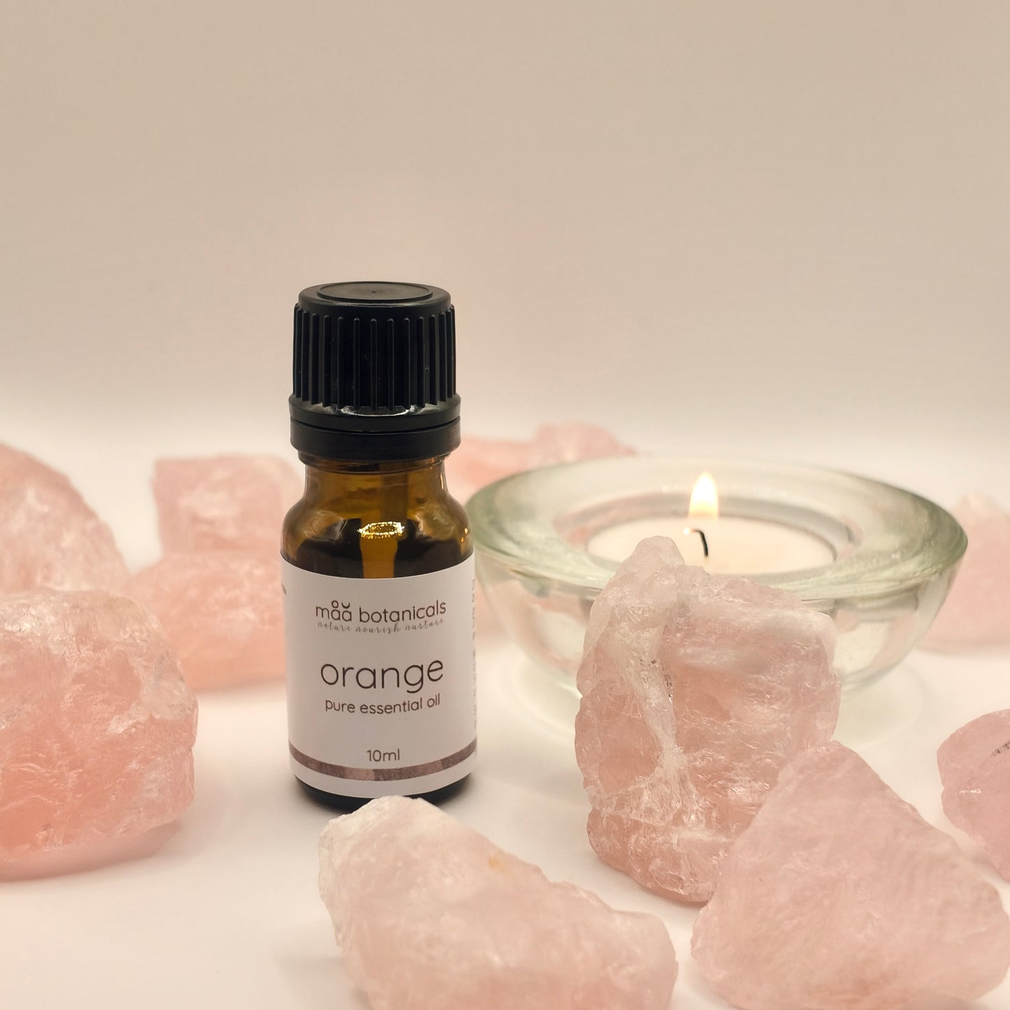 orange essential oil in a 10ml amber bottle surrounded by rose quartz crystal and a tealigt candle