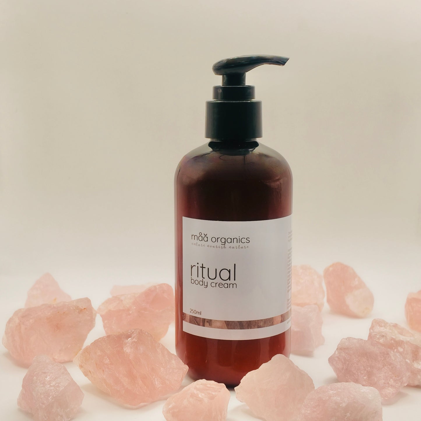 maa botanicals hand and body cream in a 250ml  amber bottle with black pump surrounded by rose quartz crystals