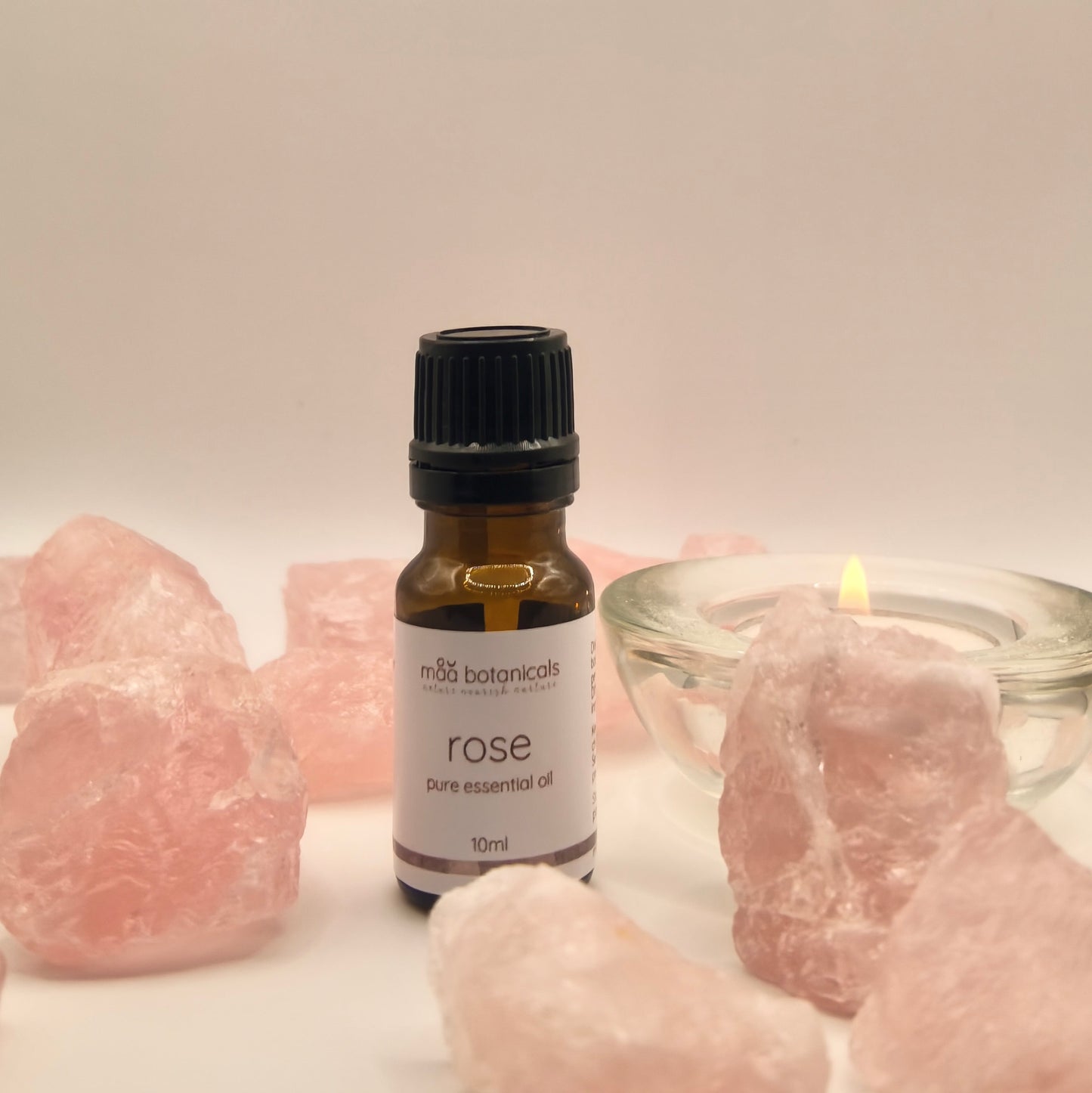 rose essential oil in a 10ml amber bottle surrounded by rose quartz crystal and a tealigt candle