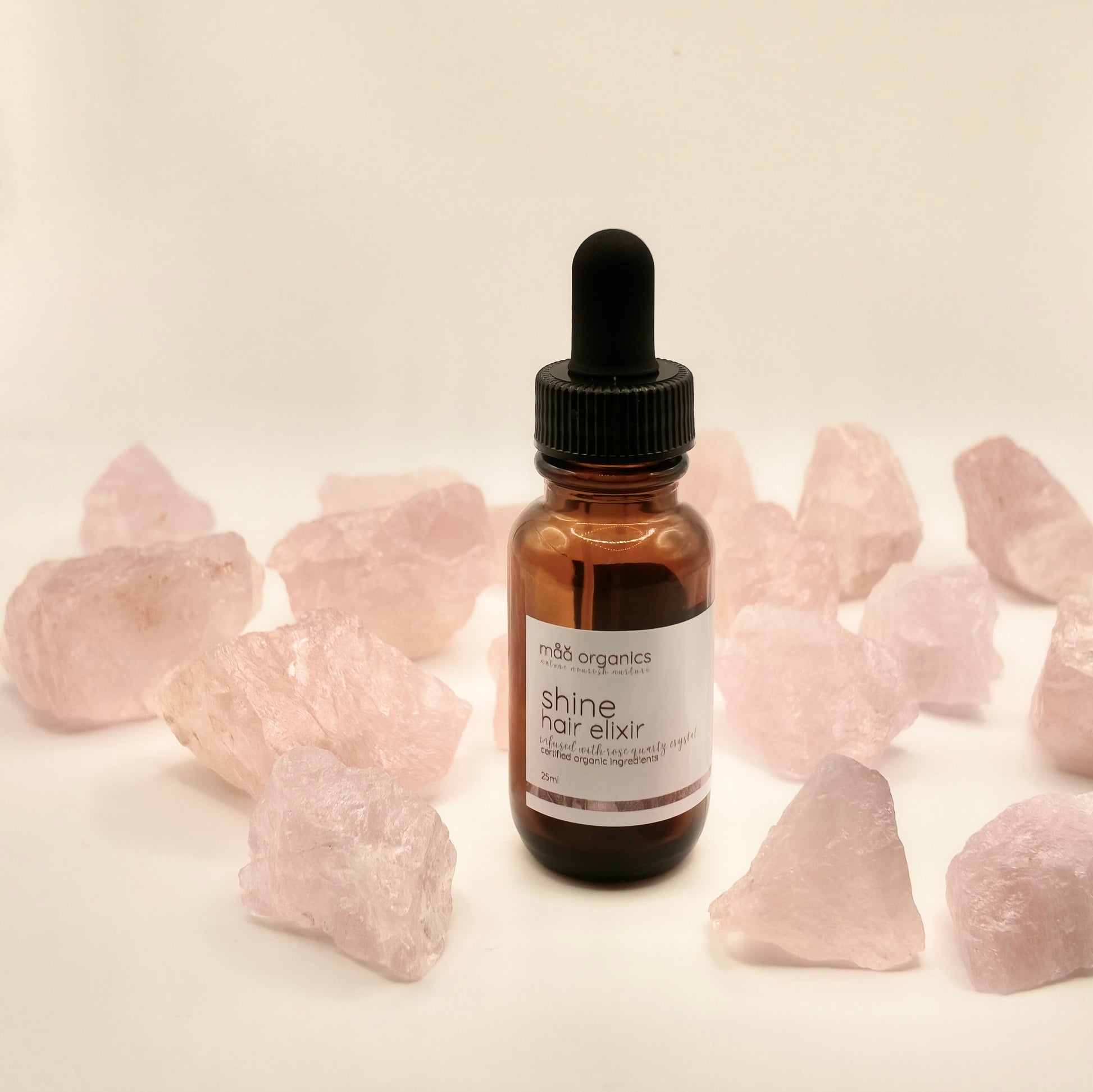 maa botanicals shine hair elixir in an 25ml amber bottle with dropper surrounded by rose quartz crystals