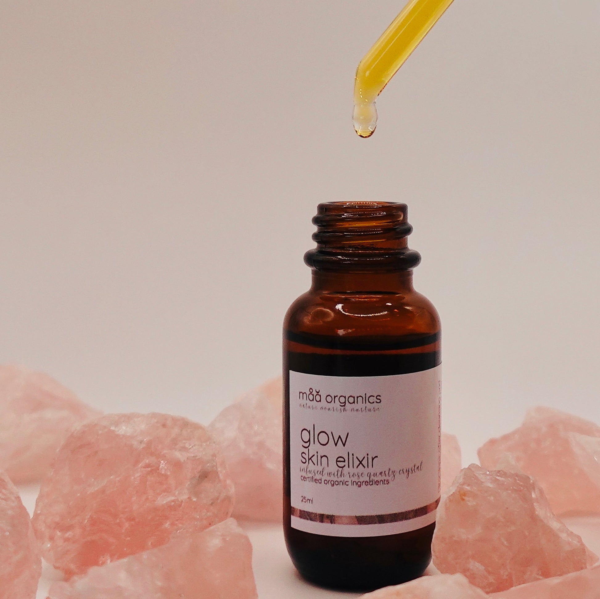 glow skin elixir with a dropper surrounded by rose quartz crystals 
