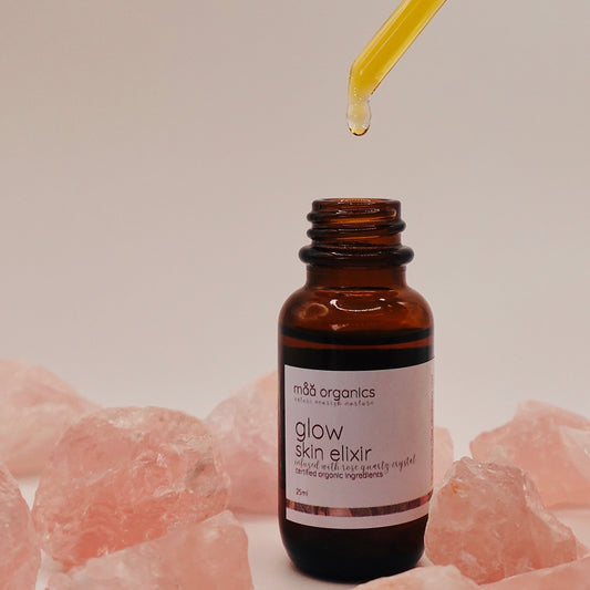 glow skin elixir with a dropper surrounded by rose quartz crystals 
